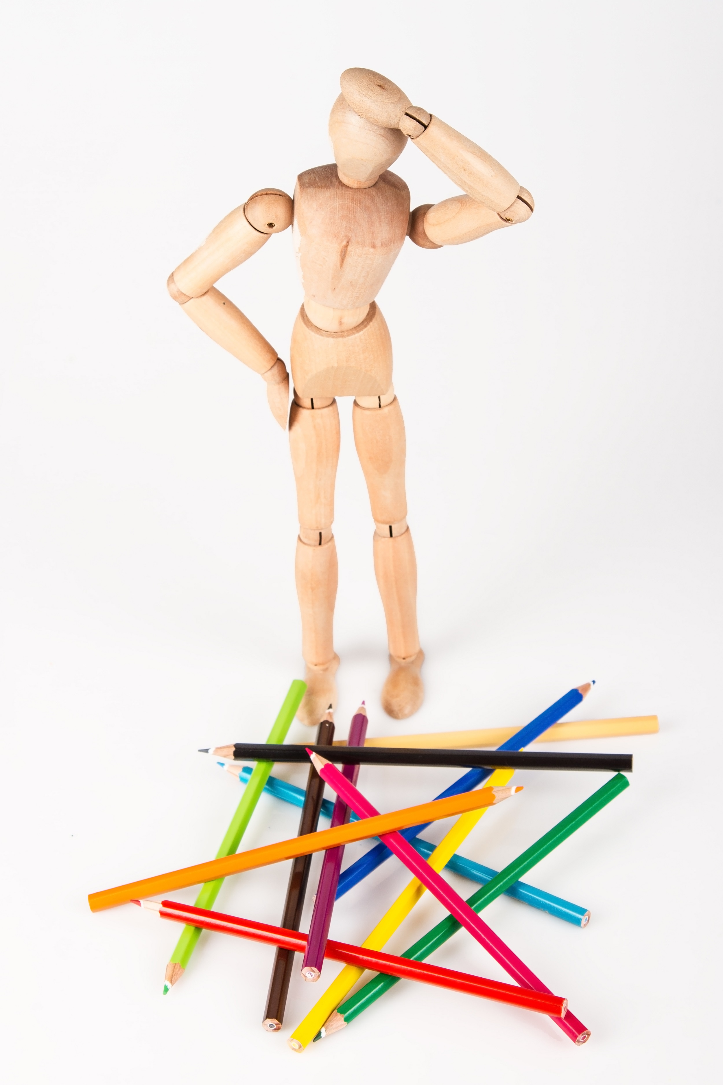 Confused wood mannequin standing at heap of colour pencil isolated on white background