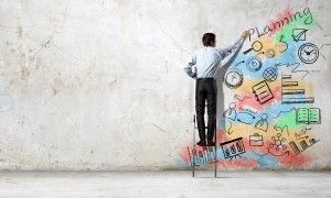 Back view of businessman standing on ladder and drawing sketches on wall